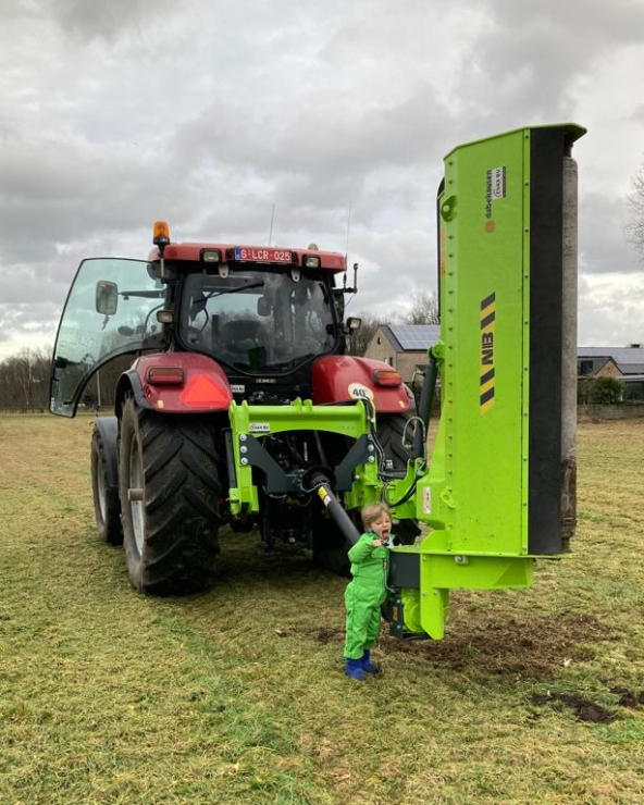 Kind in groene outfit bij rode tractor op veld.