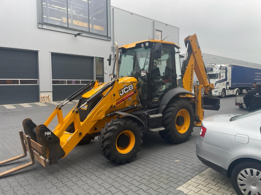 Gele graafmachine geparkeerd bij industrieel gebouw.