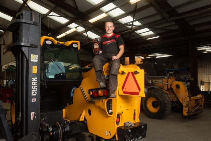 Jonge monteur met gereedschap op graafmachine in werkplaats