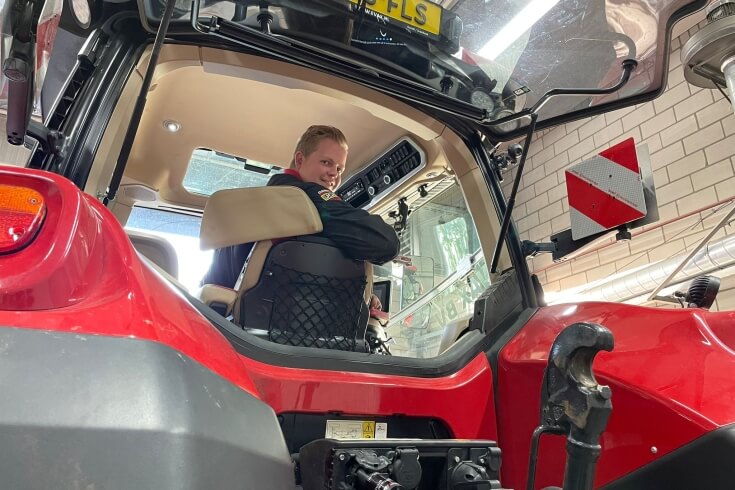 Man zit in rode tractor cabine in werkplaats.