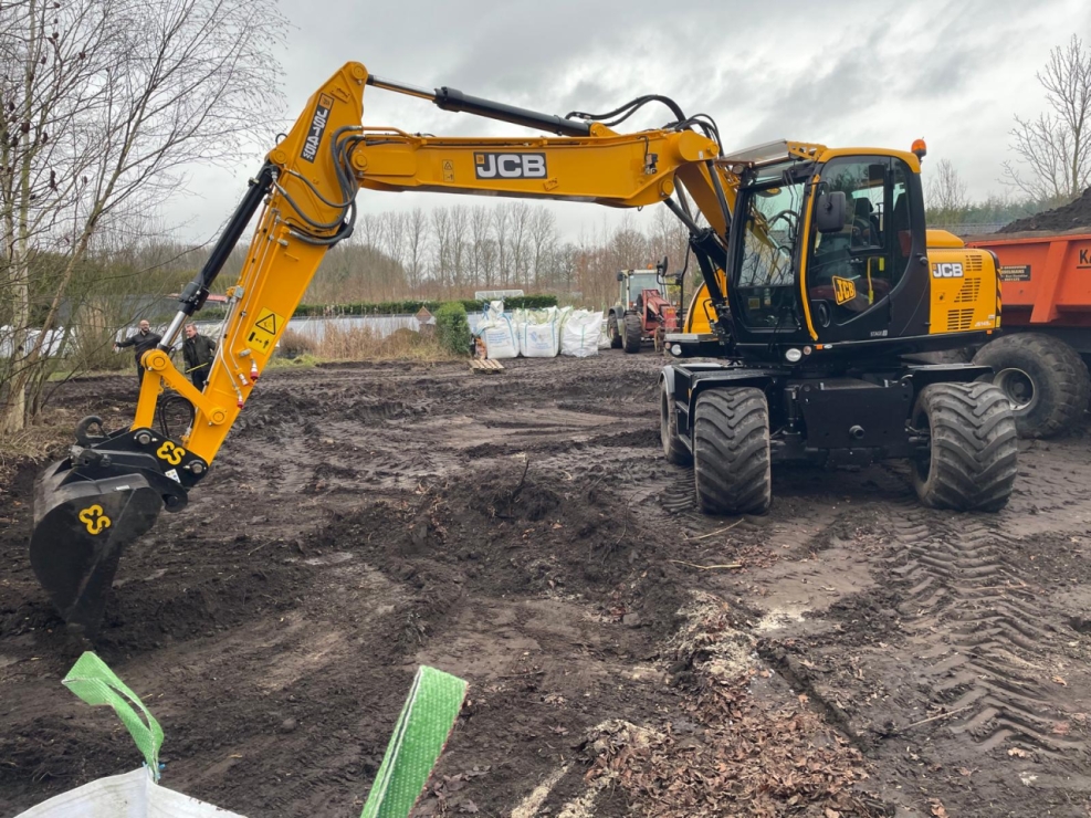 Graafmachine werkt op bouwterrein bij bewolkte lucht.