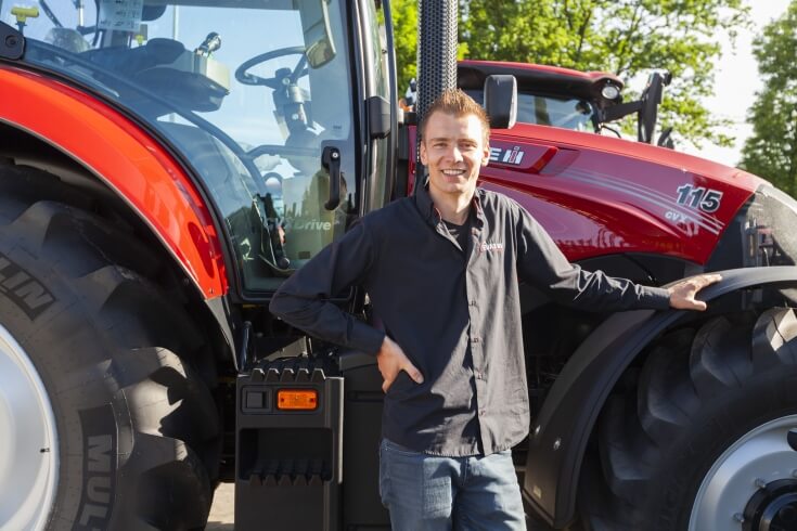Man leunt tegen grote rode tractor buiten.