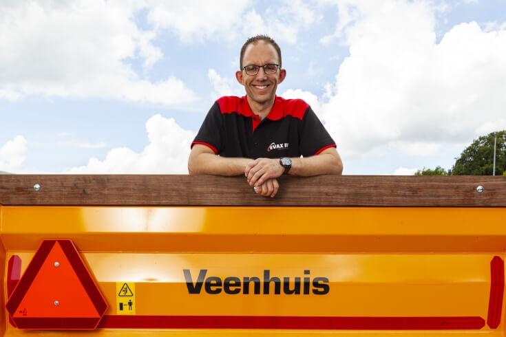 Man bij geel Veenhuis-voertuig met blauwe lucht.