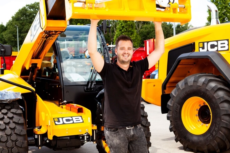 Man bij gele bouwmachines op werkplaats.