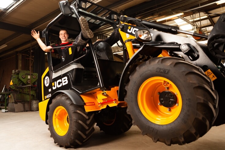 Man op een gele bouwvoertuig in werkplaats